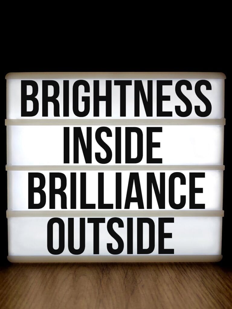 Lightbox sign with motivational message 'Brightness Inside Brilliance Outside' on a woodgrain background.