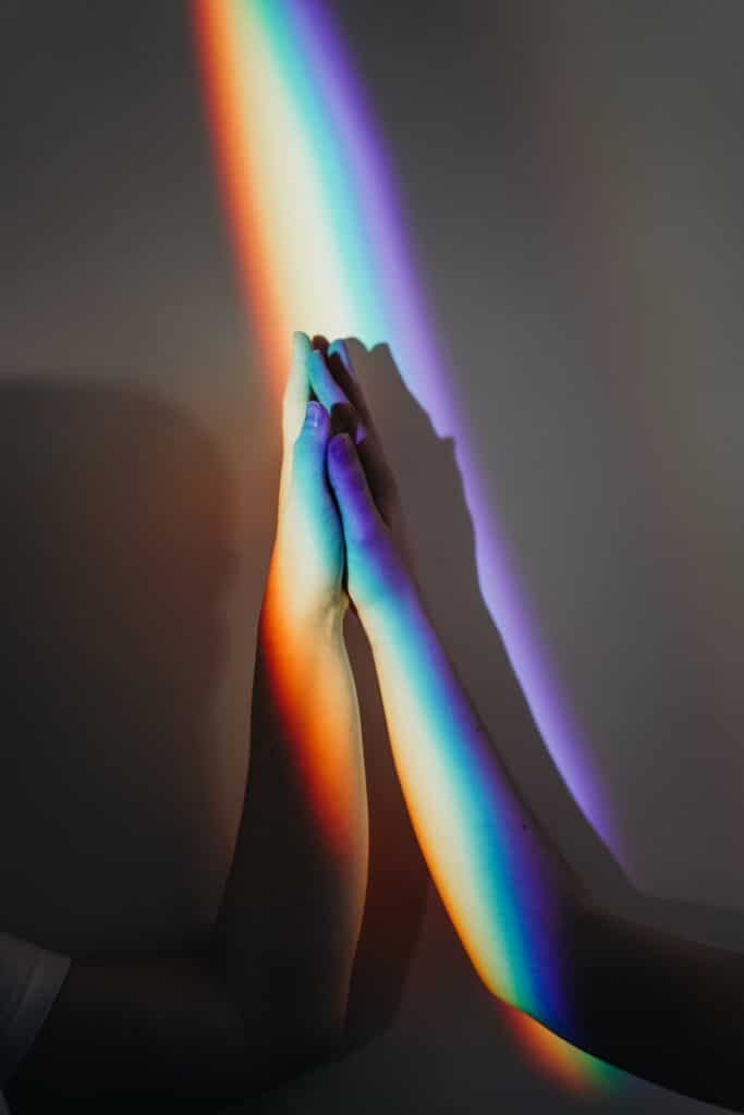 Photo by cottonbro studio Two diverse hands touch under a rainbow light symbolizing unity and diversity.