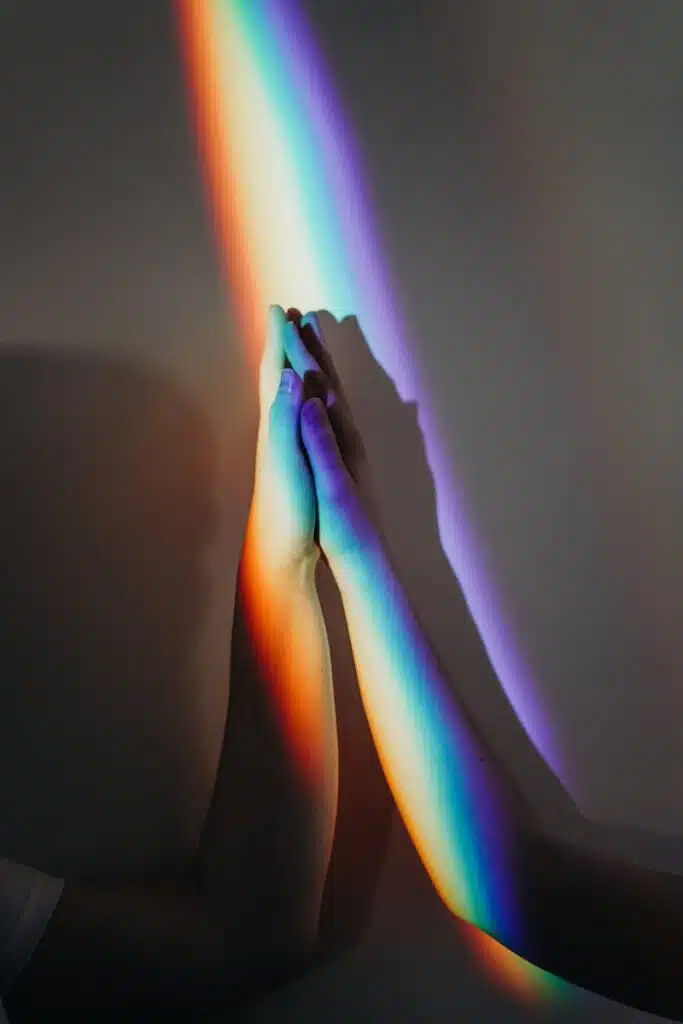 Two diverse hands touch under a rainbow light symbolizing unity and diversity.