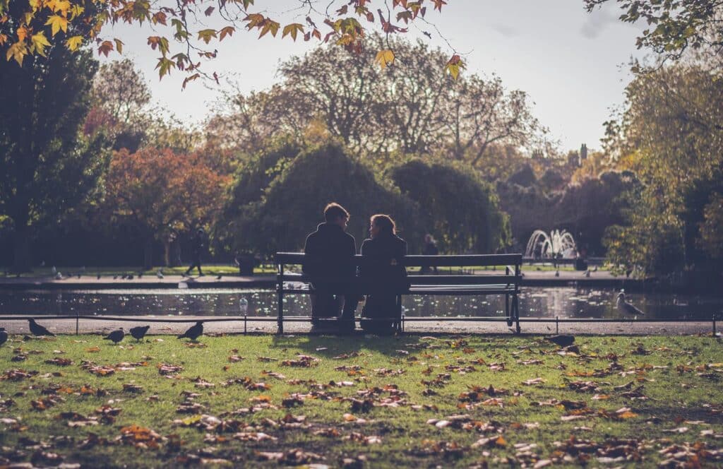 A romantic couple sitting on a park bench in Dublin during autumn with fallen leaves and scenic nature.
