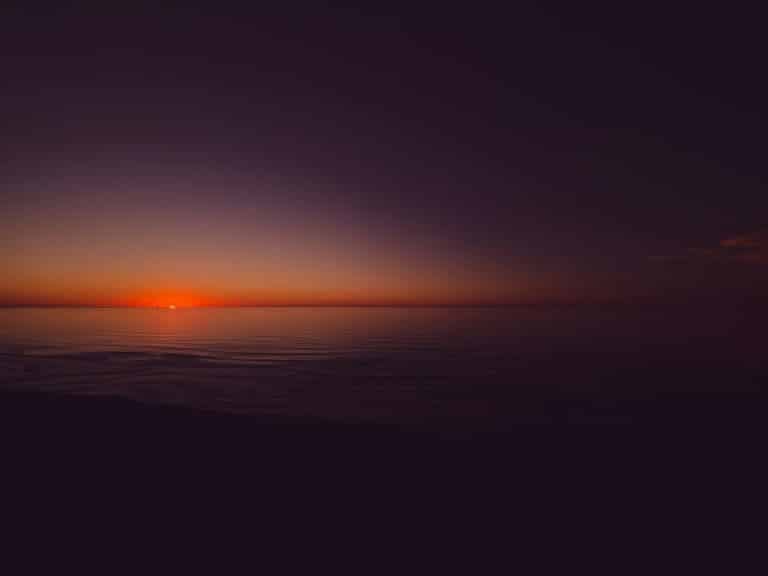 the sun is setting over the ocean on a cloudy day