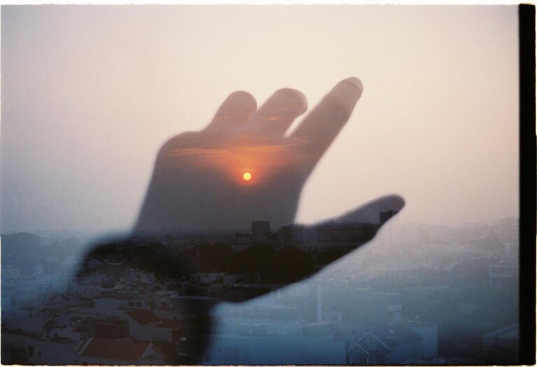 A creative montage blending a hand with a cityscape at sunset, evoking a surreal mood.