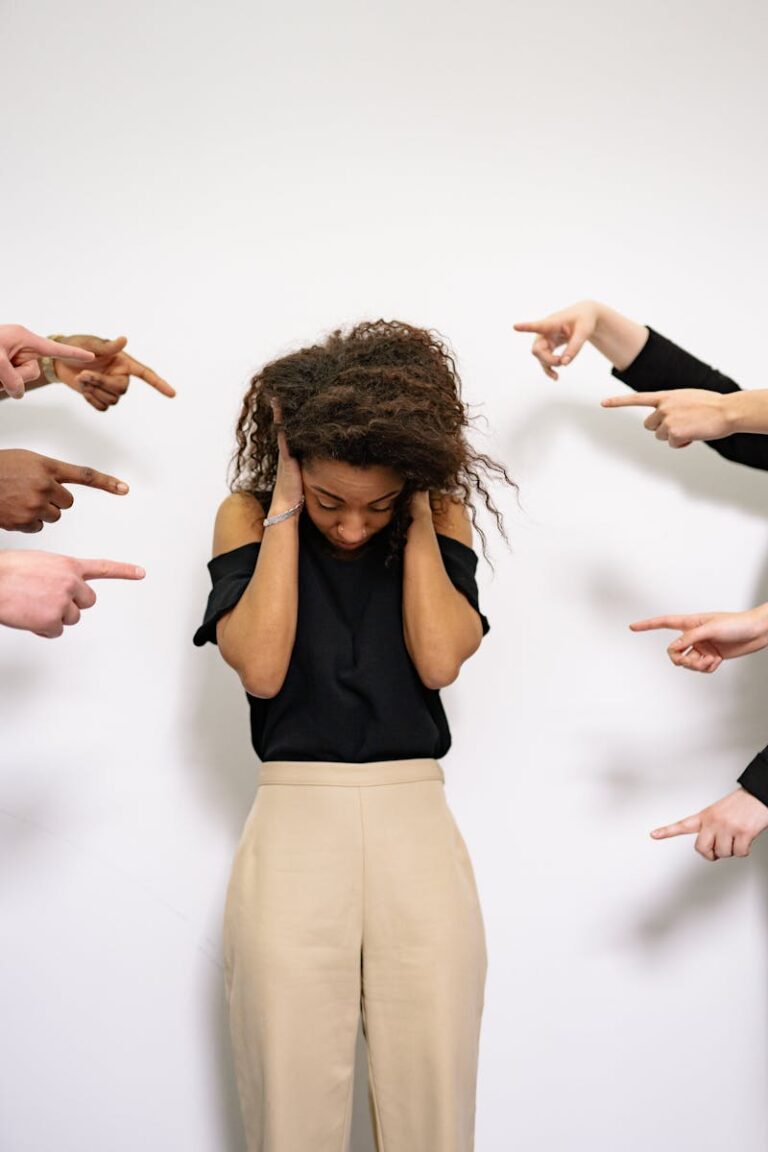 A woman overwhelmed, surrounded by pointing fingers, depicting bullying.