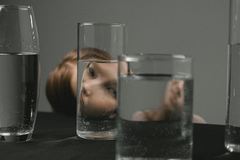 Artistic portrait of a woman’s reflection through drinking glasses on a table.